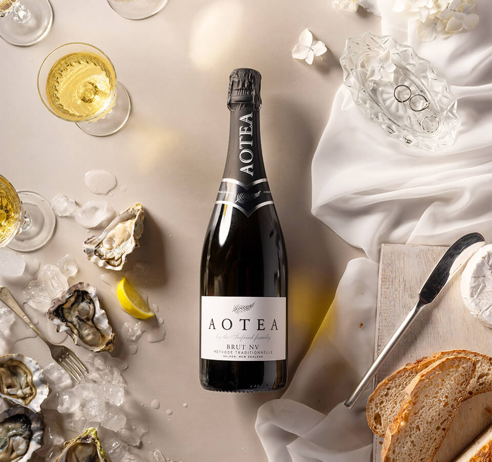 Top-down view of Aotea Nelson Brut Méthode Traditionnelle bottle styled with fresh oysters, crusty bread, and brie cheese