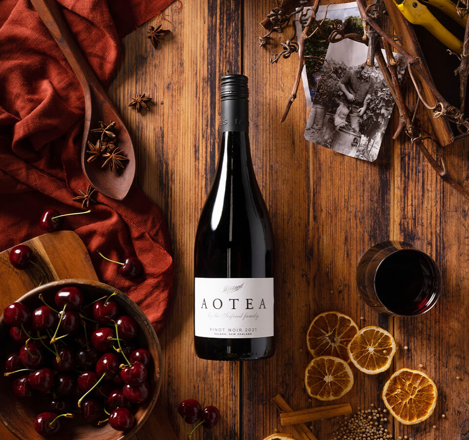 Top-down view of Aotea Nelson Pinot Noir  2021 bottle styled with fresh cherries, dried orange slices, and star anise