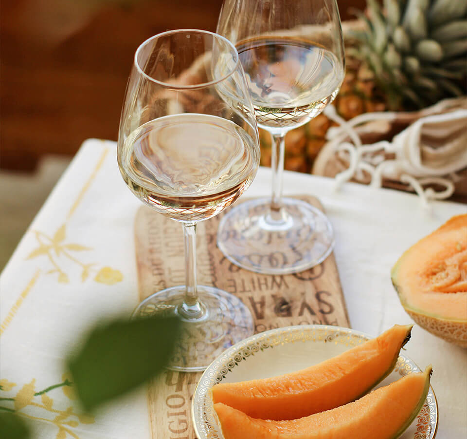 Two glasses of Old Coach Road Pinot Gris white wine styled with cantaloupe melon slices on a table