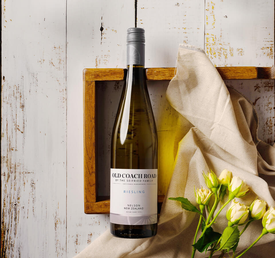 Bottle of Old Coach Road Riesling styled in a wooden tray with white roses and draped linen
