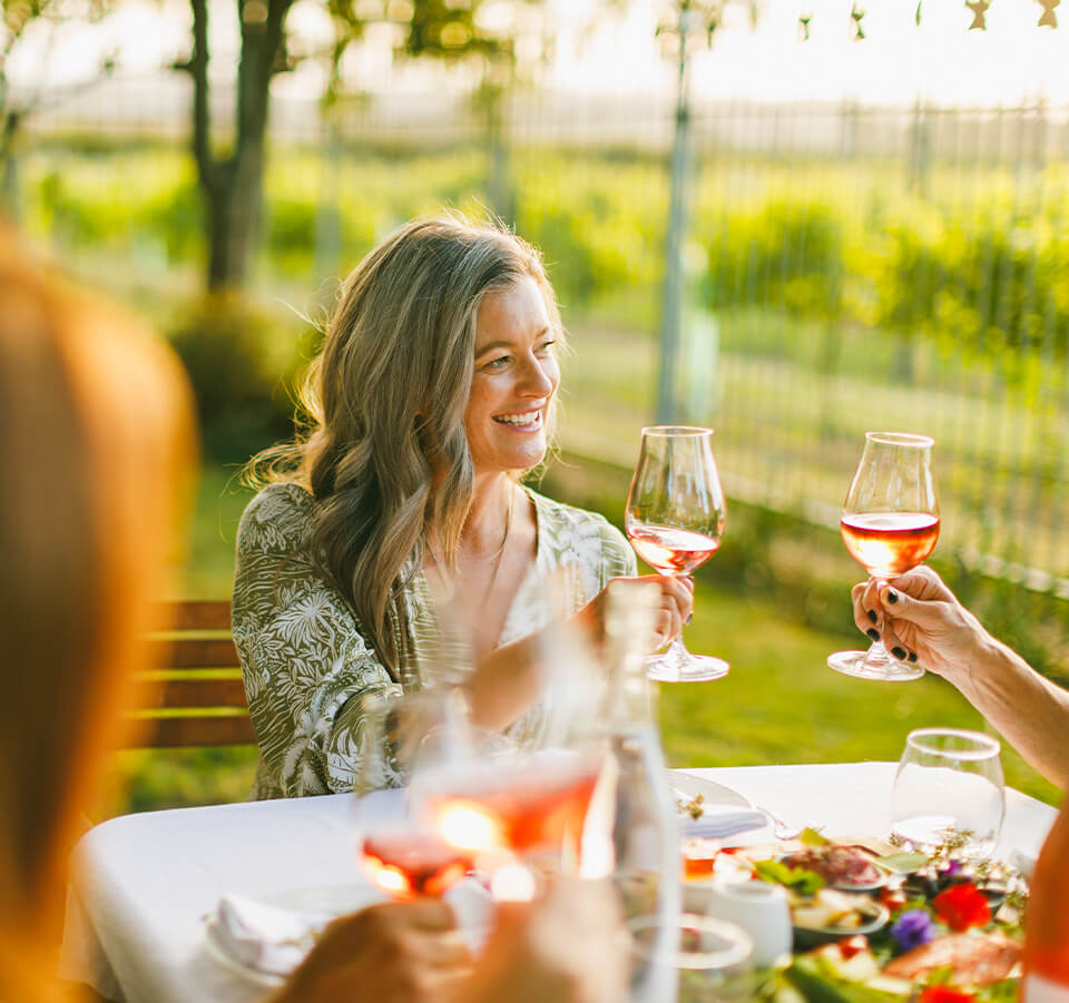 Smiling woman holding a glass of Old Coach Road Rosé wine during an outdoor toast