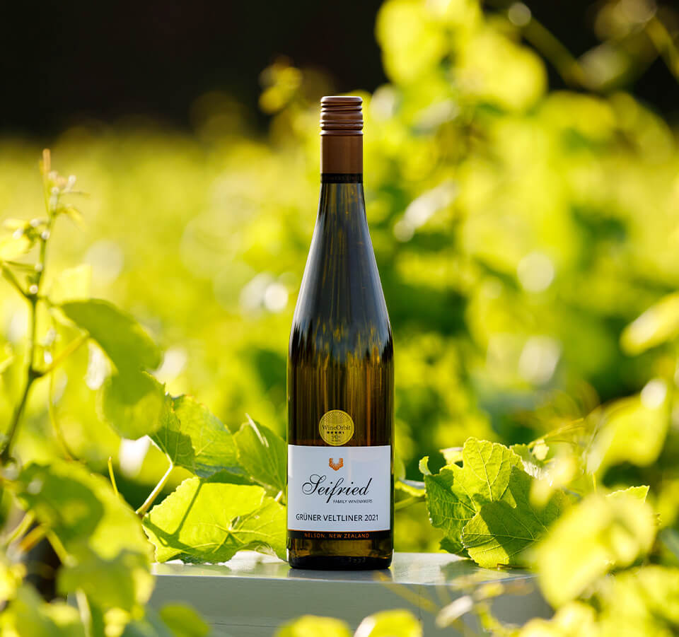 Bottle of Seifried Nelson Grüner Veltliner 2021 standing outdoors among sunlit vineyard grapevines