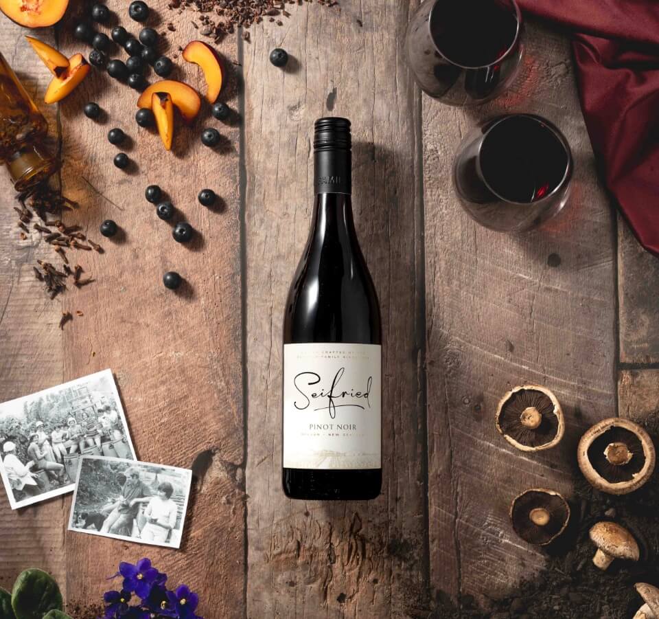 Bottle of Seifried Nelson Pinot Noir styled with fresh dark cherries and subtle spice to highlight its rich red fruit flavours