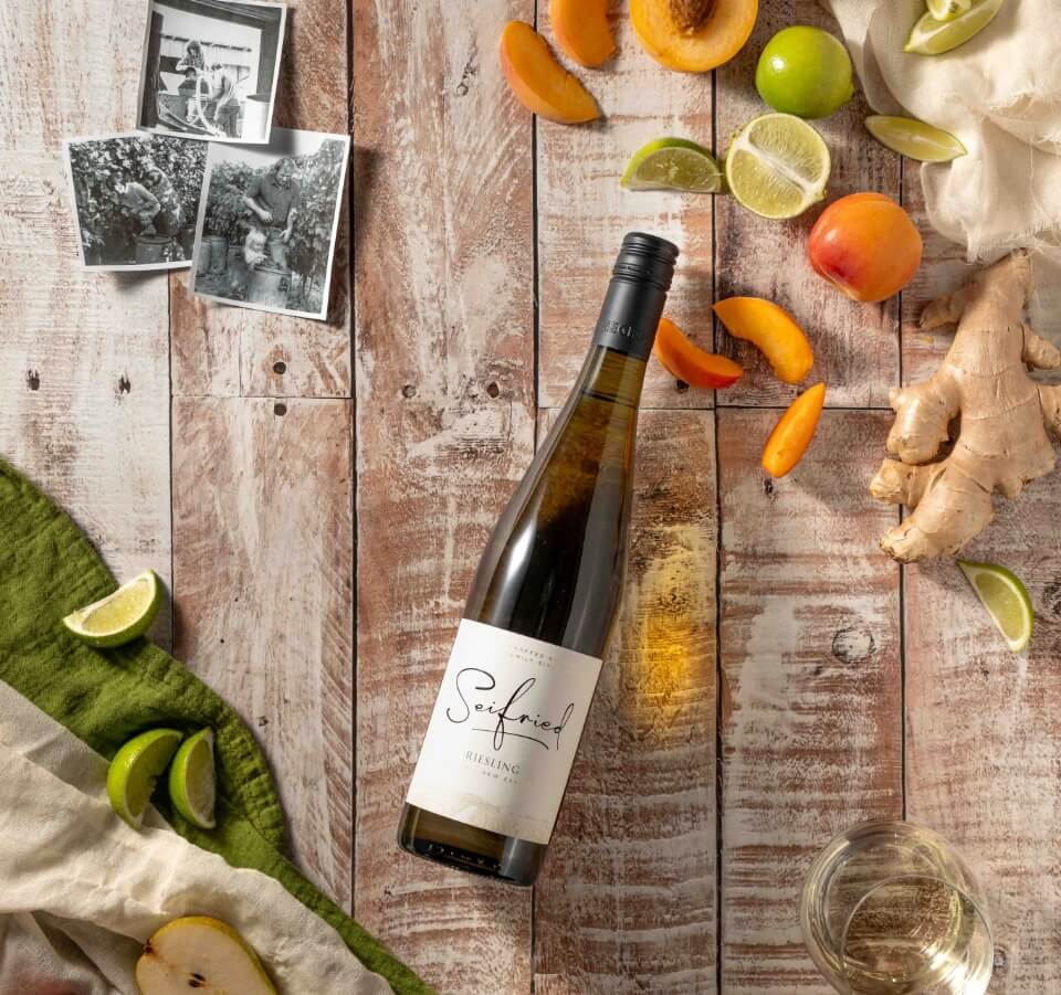 Bottle of Seifried Nelson Riesling styled with fresh green apples, limes, and white floral blossoms to highlight its crisp citrus flavours