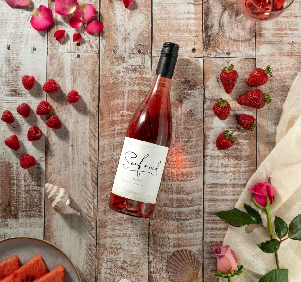 Bottle of Seifried Nelson Rosé on a wooden table, styled with fresh strawberries, raspberries, and rose petals to highlight its fruit flavours