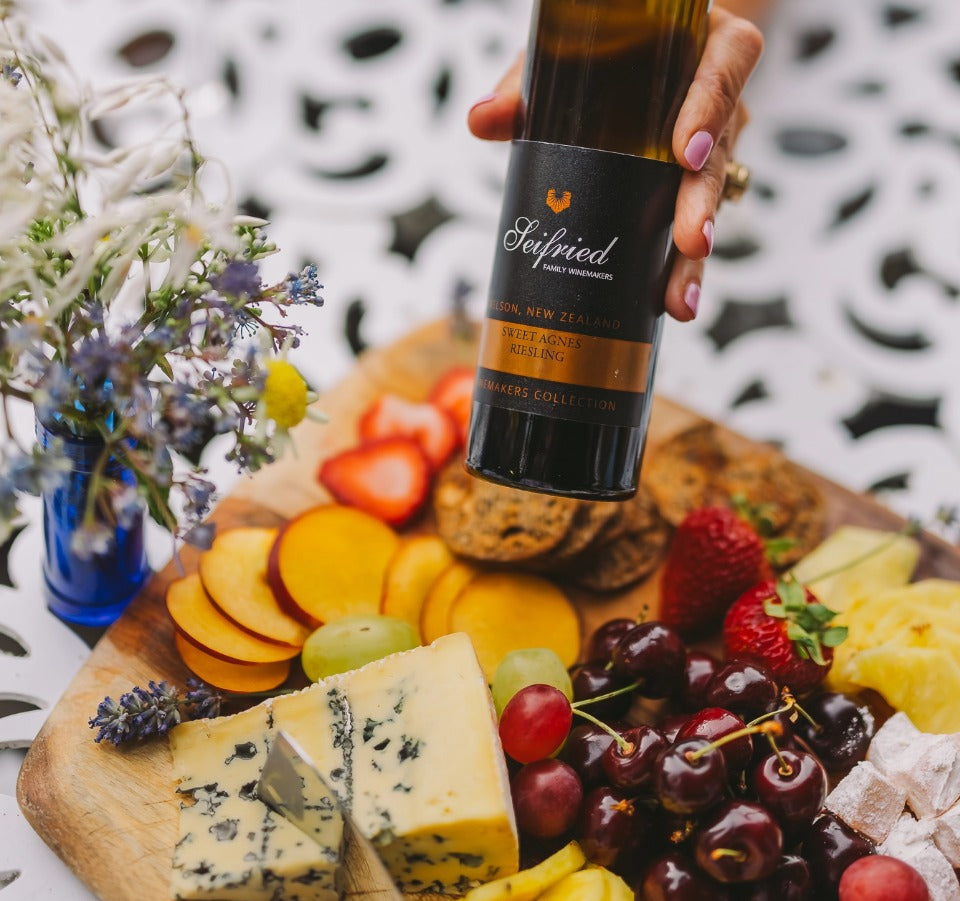 Bottle of Sweet Agnes Riesling alongside a cheese platter of assorted fruit and cheese