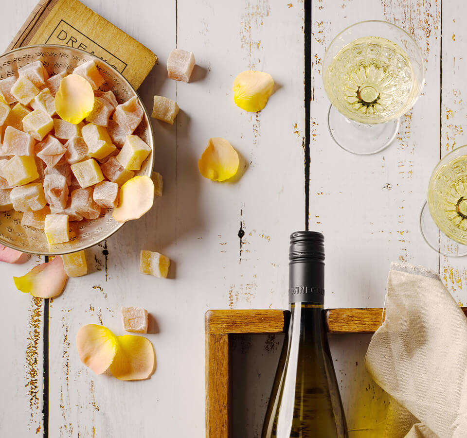 Flatlay of Cellar Release Seifried Winemakers Collection Nelson Gewürztraminer with wine glasses, yellow rose petals, and Turkish delight